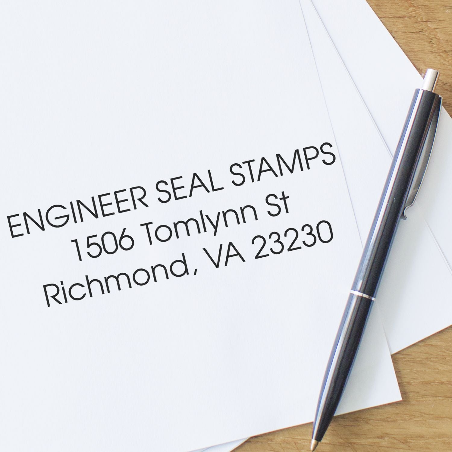 3 Line Address Stamp - Regular Rubber Stamp imprint on white paper with a pen beside it, displaying an address: 1506 Tomlynn St, Richmond, VA 23230.