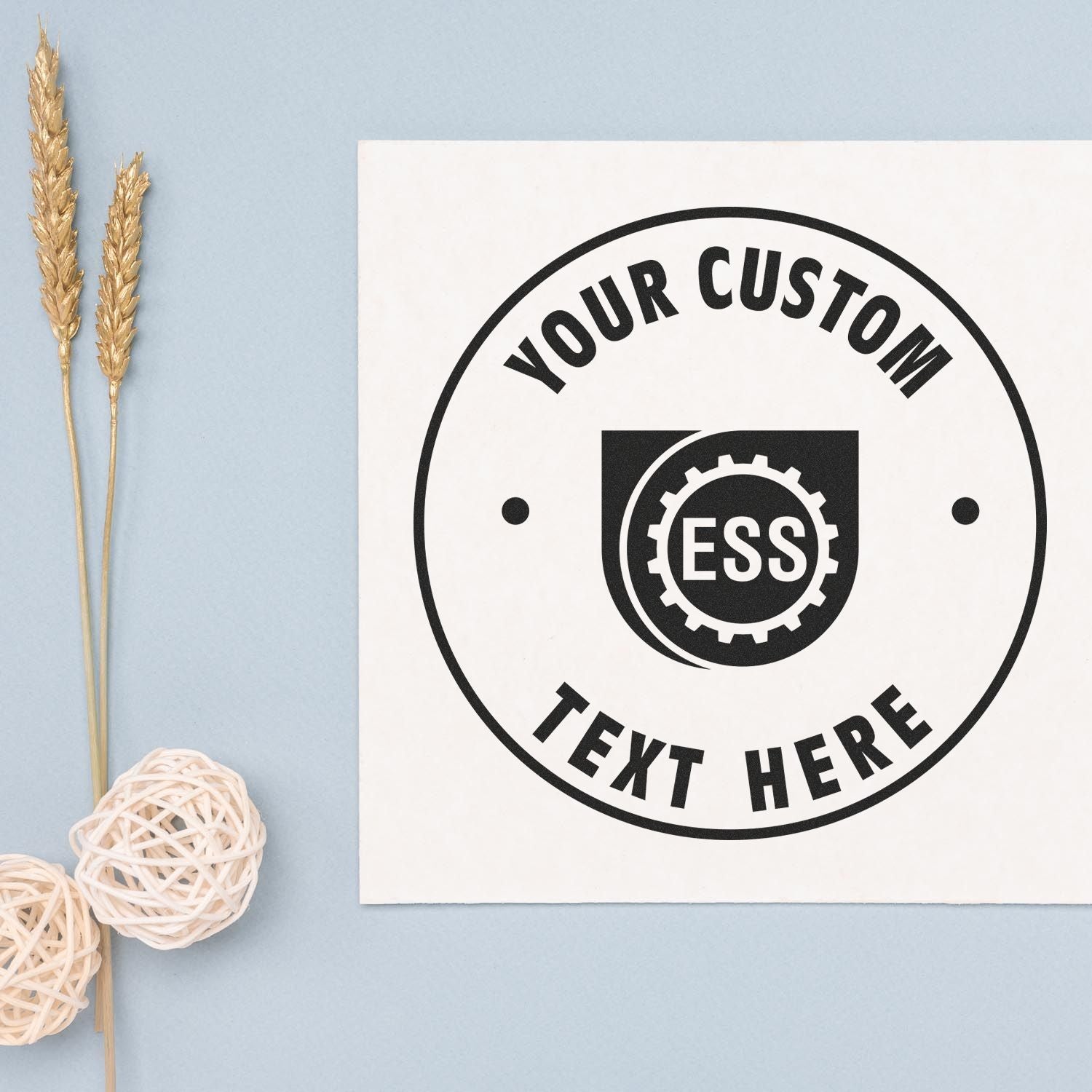 Custom Rubber Stamp Size 1-1/2 Inch Diameter with YOUR CUSTOM TEXT HERE and ESS logo stamped on white paper, next to decorative items.