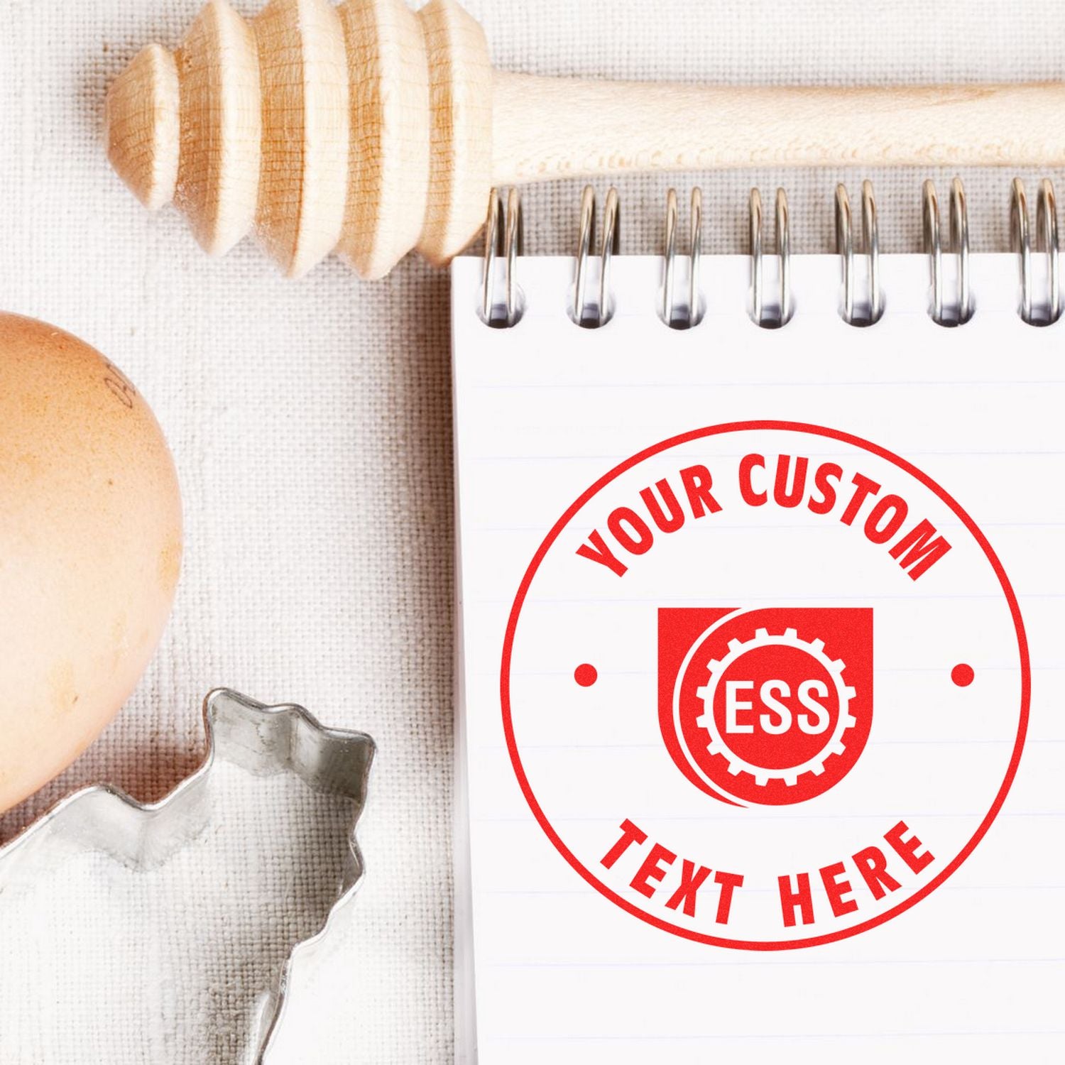 Custom Rubber Stamp Size 2-1/2 Inch Diameter with Your Custom Text Here in red ink on a spiral notebook, next to an egg and honey dipper.