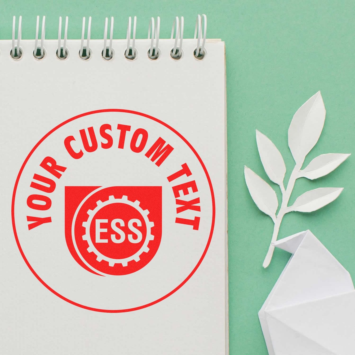 Custom Rubber Stamp Size 7 Inch Diameter imprinting YOUR CUSTOM TEXT in red on a white notepad, with a green background and paper leaves.