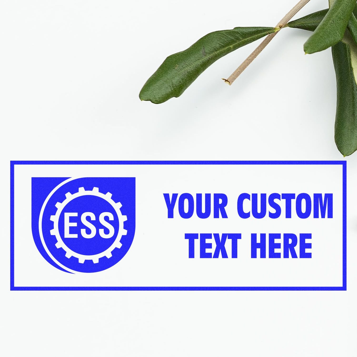 Custom Rubber Stamp Size 1 x 2 with blue ESS logo and Your Custom Text Here text, placed on a white surface with green leaves.