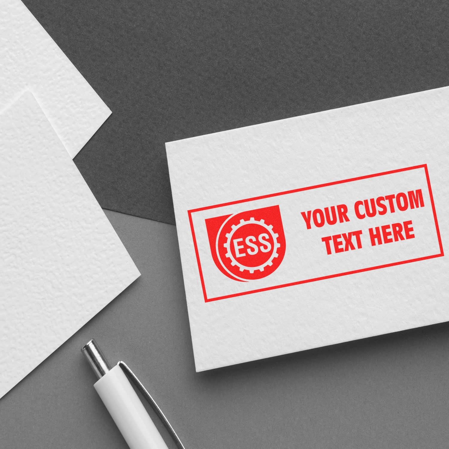 Custom Rubber Stamp Size 1 x 4 in red ink on a white card with ESS logo and YOUR CUSTOM TEXT HERE beside a white pen on a gray surface.