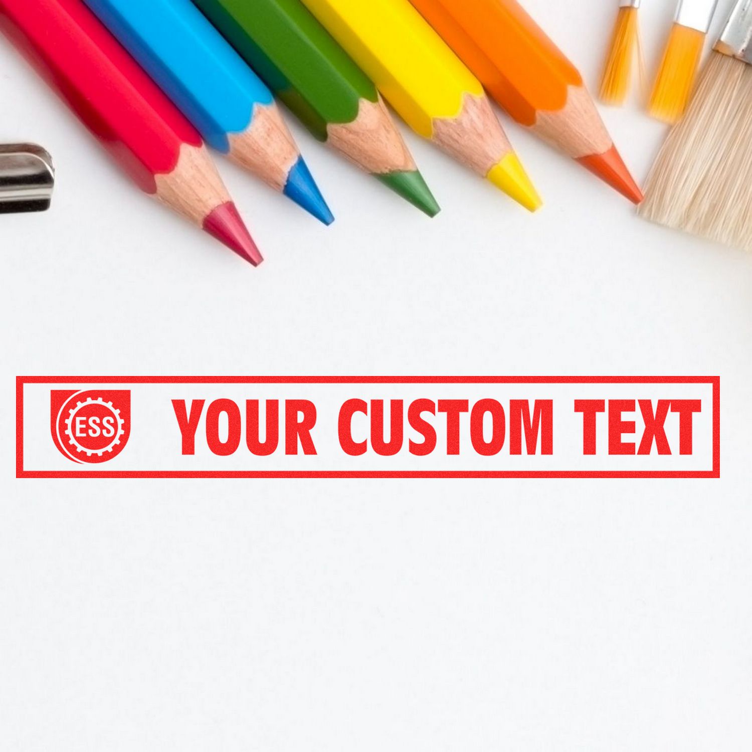 Colored pencils and paintbrushes surround a stamped message reading YOUR CUSTOM TEXT using the Custom Rubber Stamp Size 1 x 10.