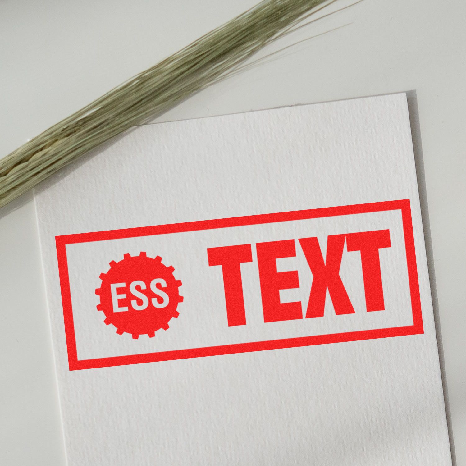 Custom Rubber Stamp Size 3 x 6 in use, displaying a bold red ESS TEXT imprint on white paper, with a plant stem nearby.