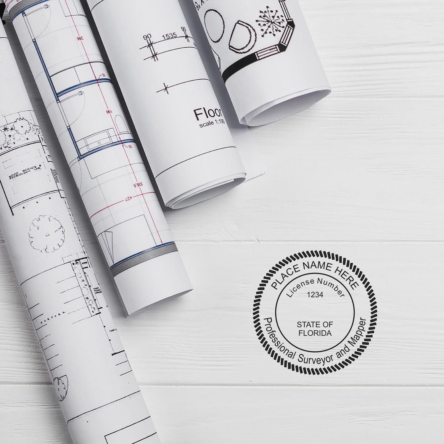 Self Inking Florida Land Surveyor Stamp on white wooden surface with rolled architectural blueprints nearby.
