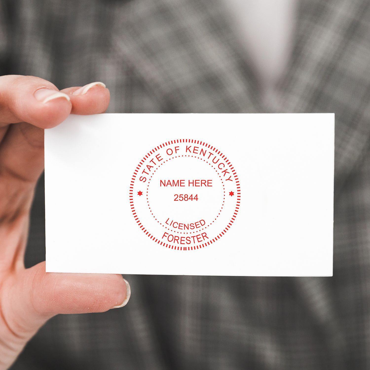 A hand holding a card stamped with the Forester Self Inking Rubber Stamp of Seal, displaying State of Kentucky and Licensed Forester.