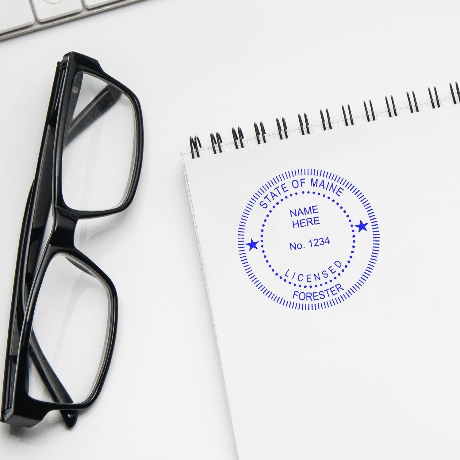 Forester Slim Pre-Inked Rubber Stamp of Seal used on a notepad next to a pair of glasses and a keyboard.