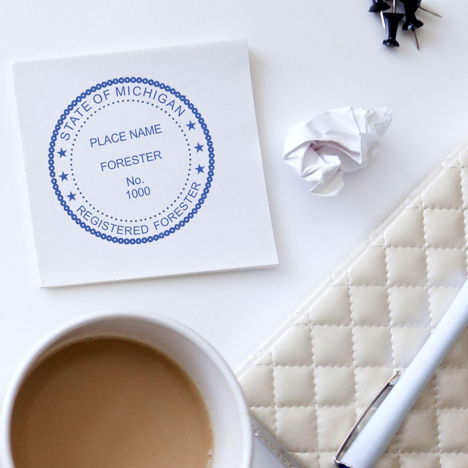 Forester Slim Pre-Inked Rubber Stamp of Seal used on paper, placed on a white desk with a coffee cup, pen, and crumpled paper nearby.