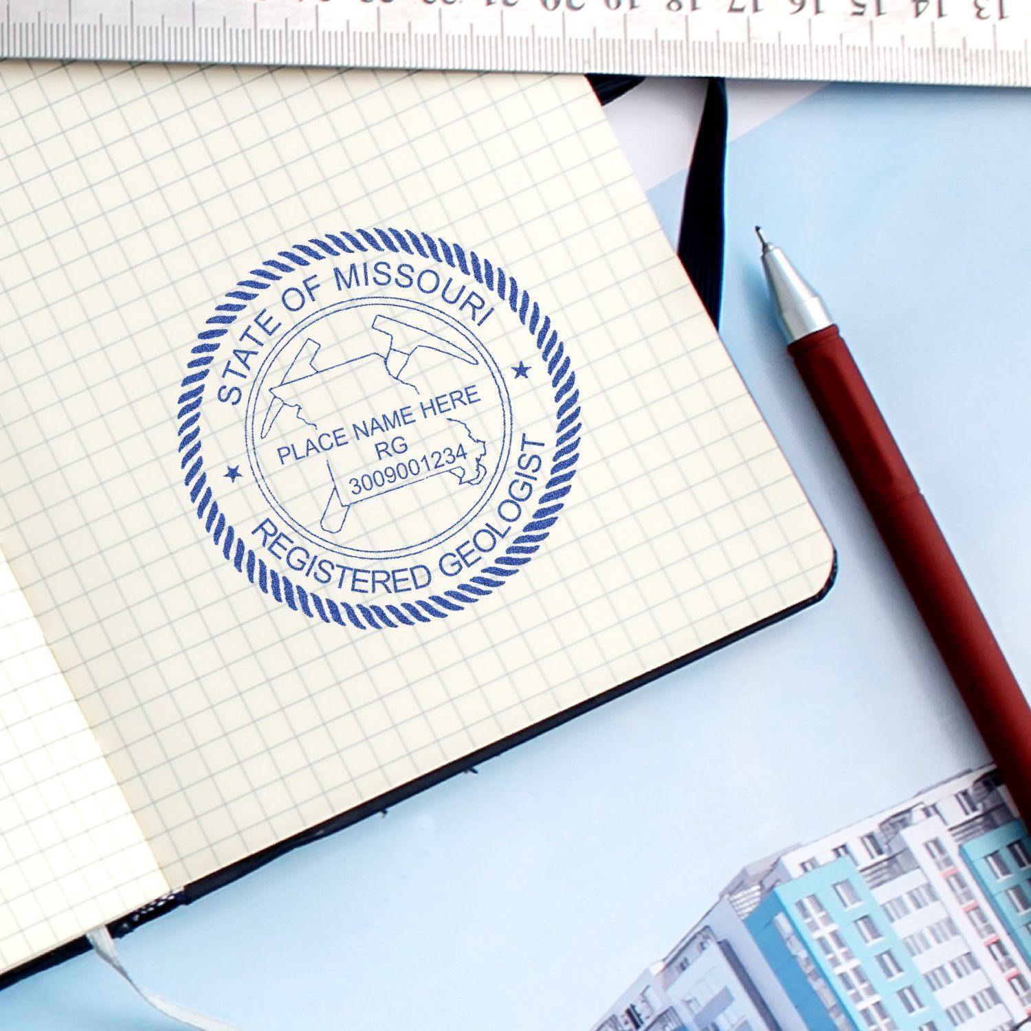 Geologist Self Inking Rubber Stamp of Seal used on a notebook, with a pen and ruler nearby. The seal reads State of Missouri Registered Geologist.