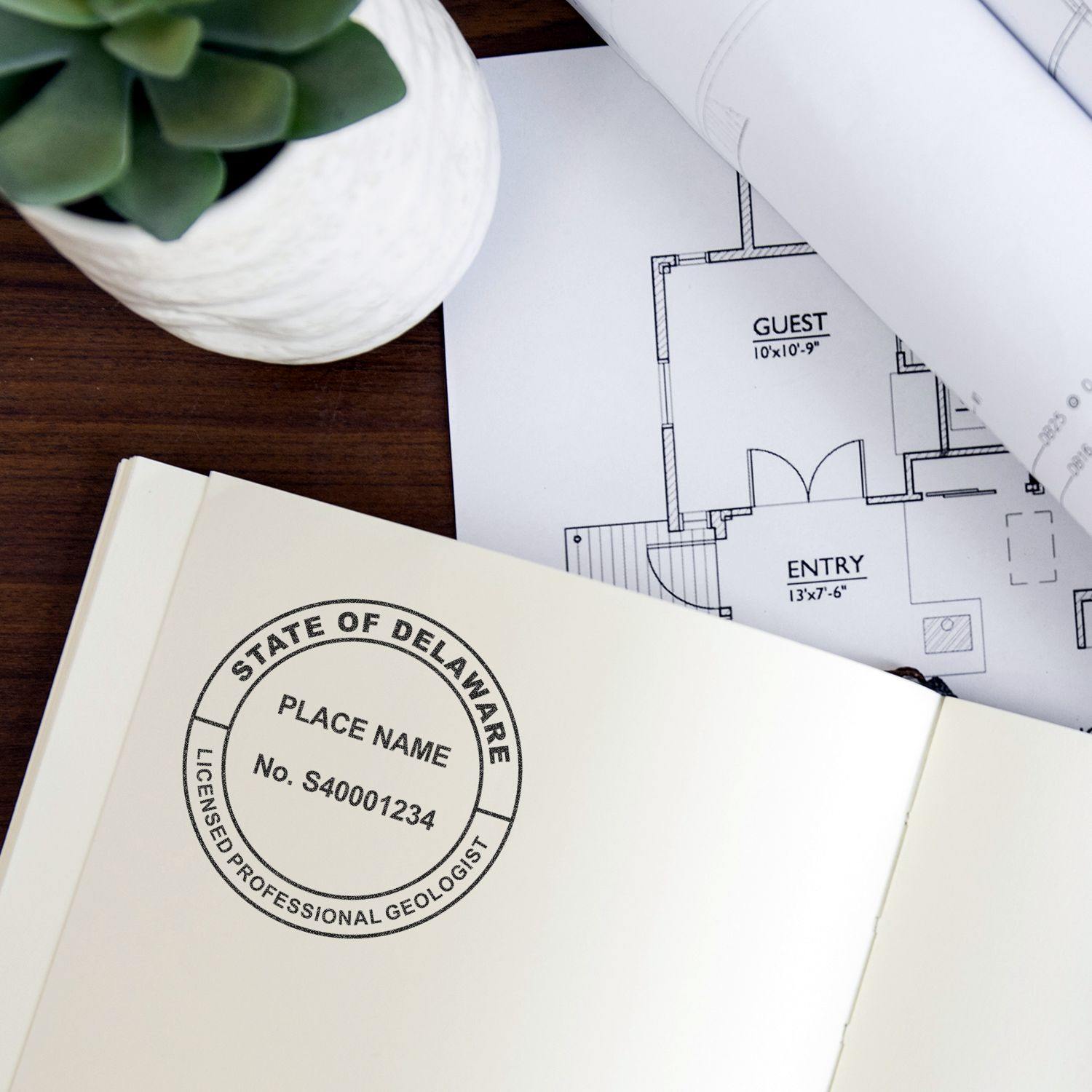 Geologist Self Inking Rubber Stamp of Seal on an open book beside architectural plans and a potted plant on a wooden desk.