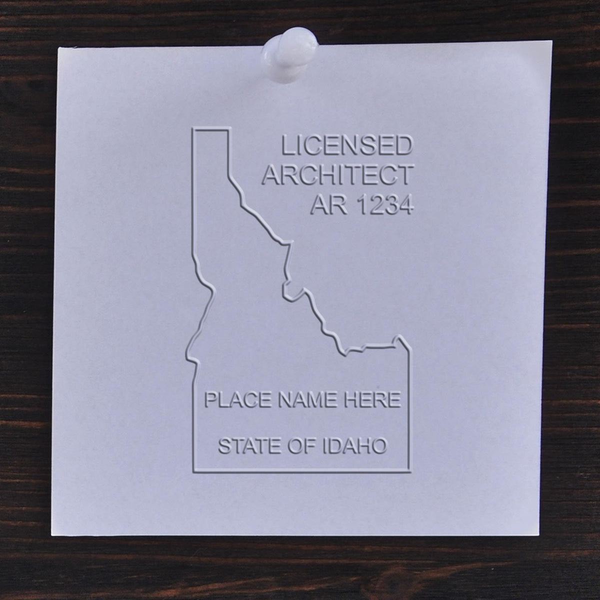 A lifestyle photo showing a stamped image of the Handheld Idaho Architect Seal Embosser on a piece of paper