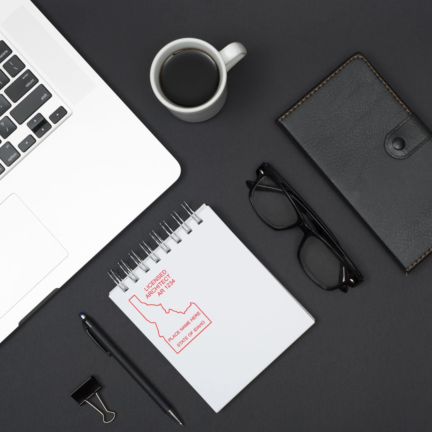 Self Inking Idaho Architect Stamp on a notepad, placed on a desk with a laptop, coffee cup, glasses, pen, and a wallet.