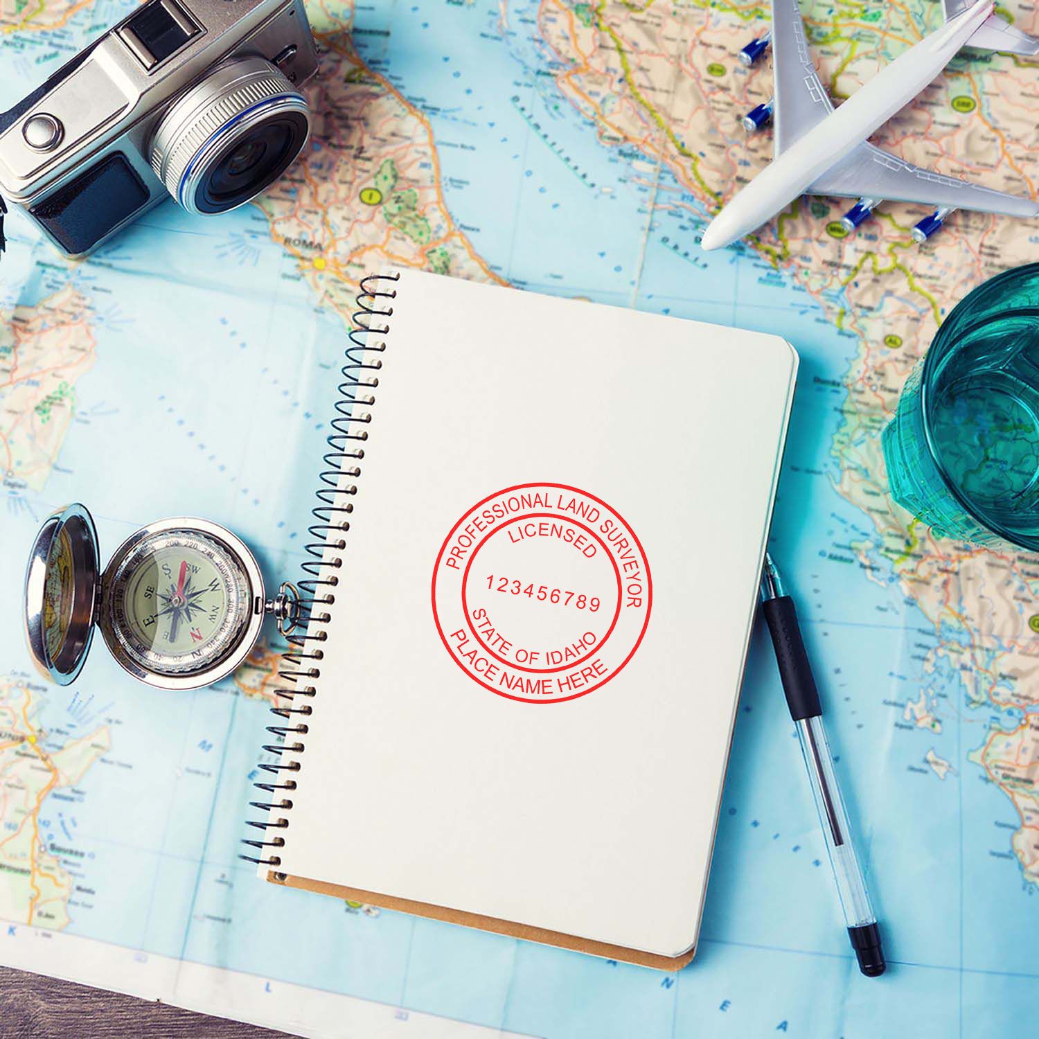 Self Inking Idaho Land Surveyor Stamp on a notebook, surrounded by a compass, pen, camera, and a map.