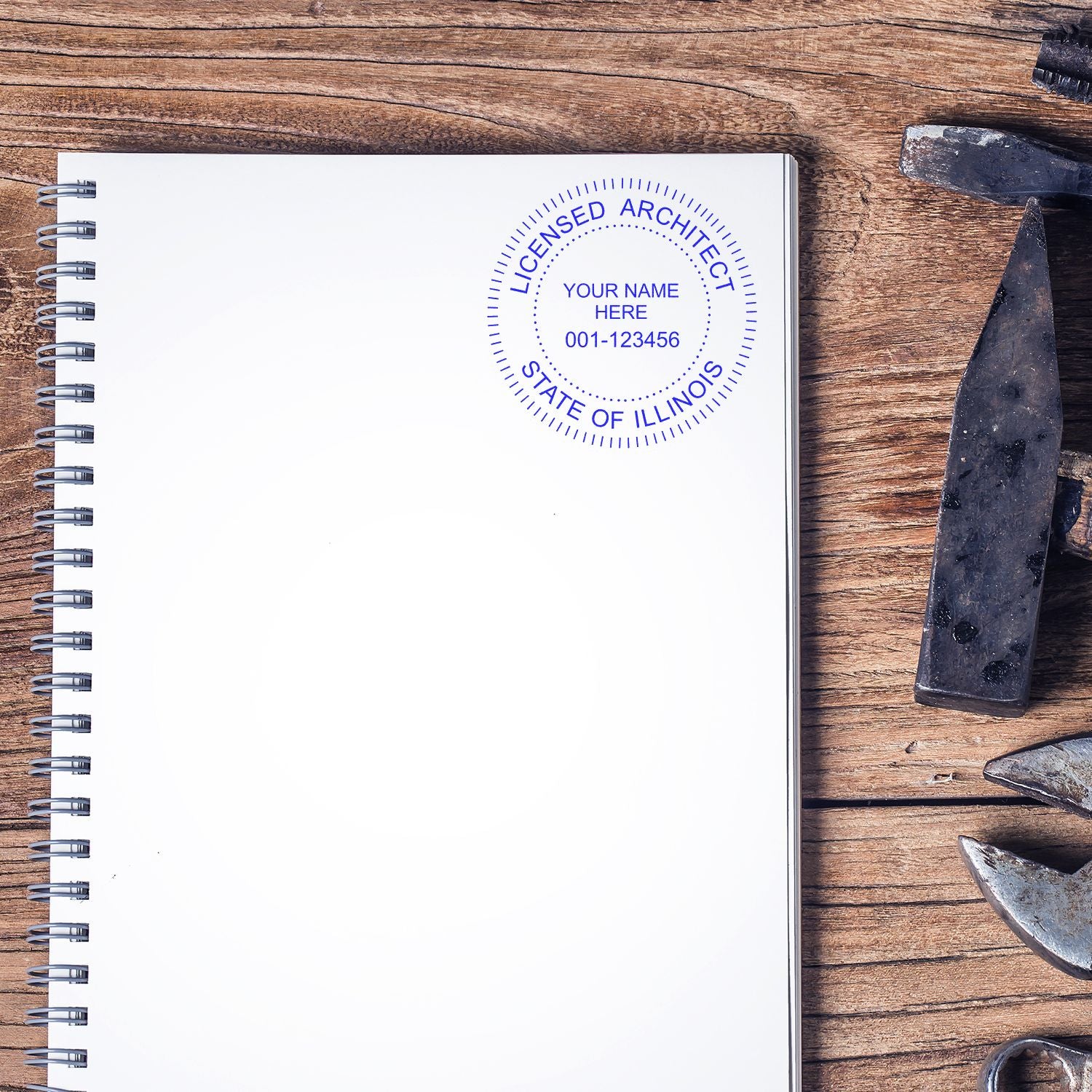 Self Inking Illinois Architect Stamp on a blank notebook page, surrounded by tools on a wooden surface.