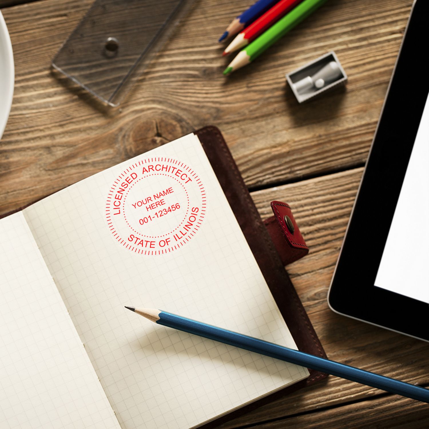 Self Inking Illinois Architect Stamp on an open notebook with a pencil, tablet, and colorful pencils on a wooden desk.