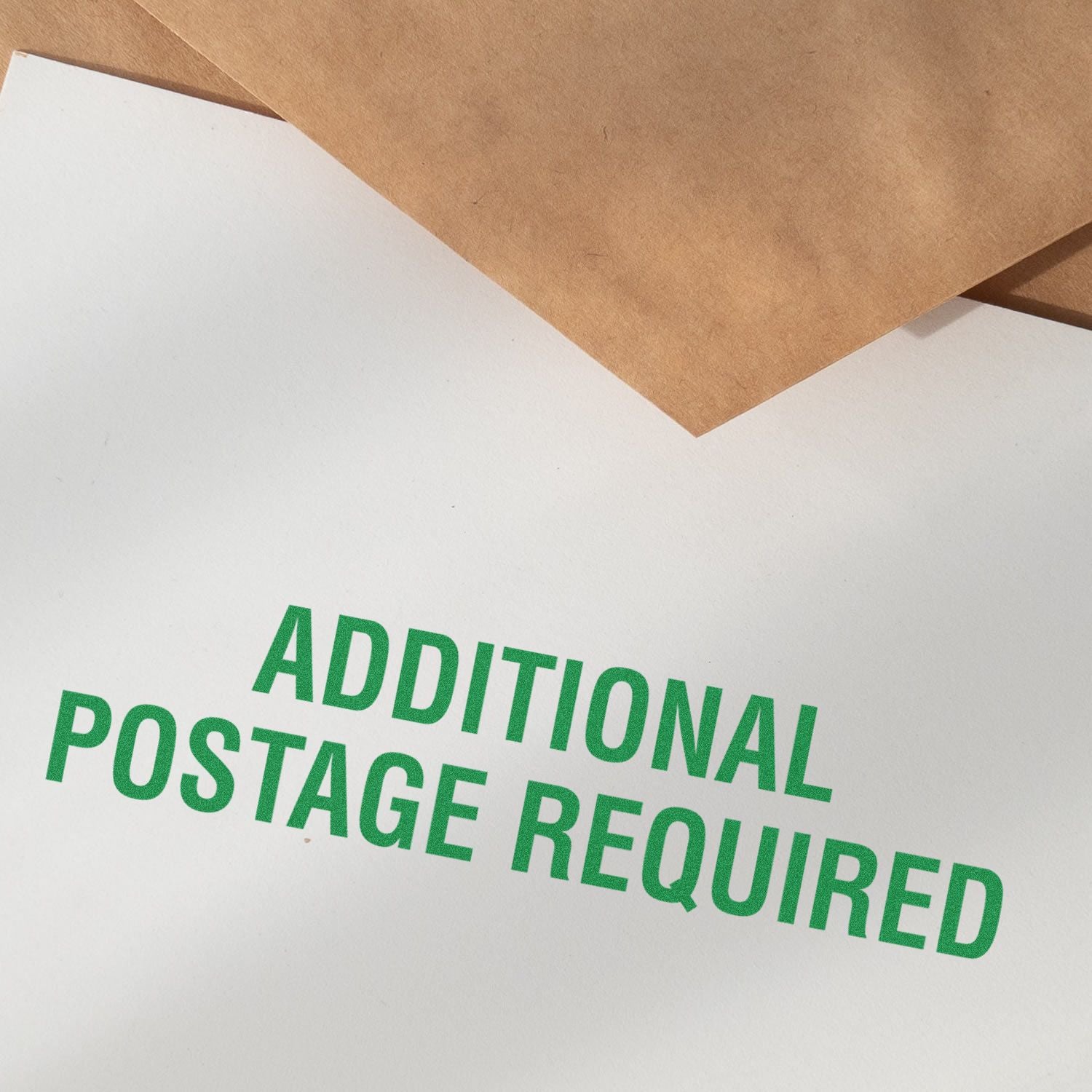Additional Postage Required rubber stamp impression in green ink on white paper, with brown envelopes in the background.