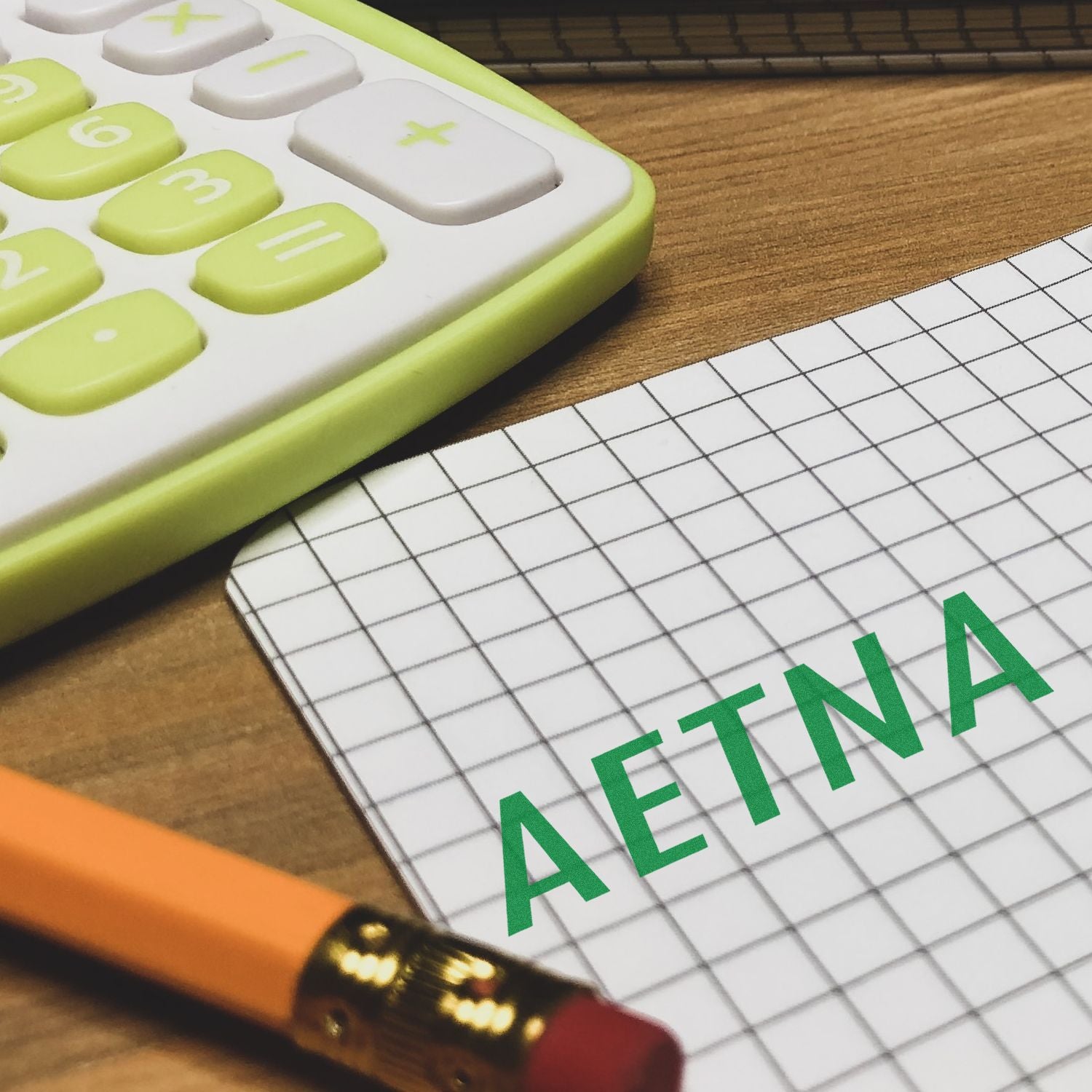 Slim Pre-Inked Aetna Stamp used on graph paper, with a yellow calculator and pencil nearby on a wooden desk.