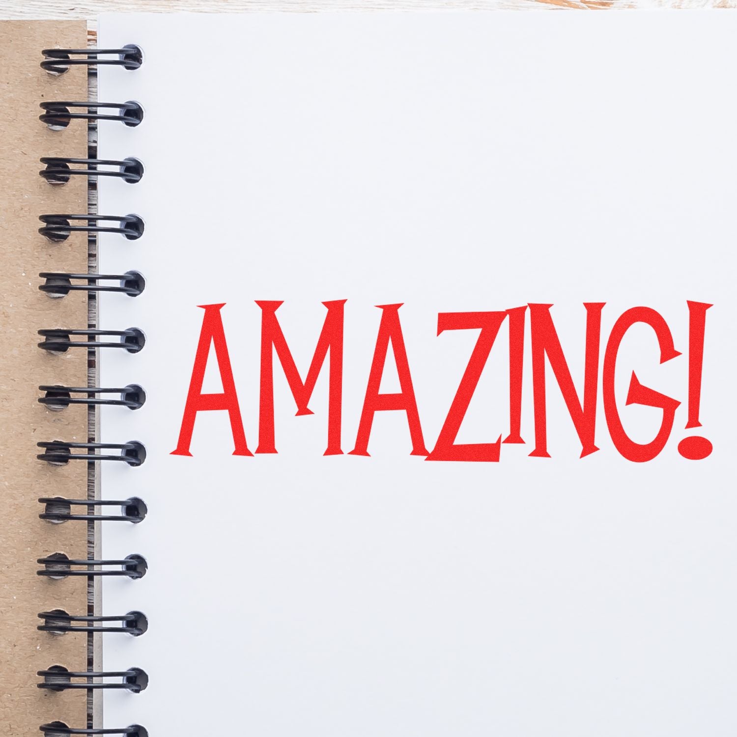 A notebook with a spiral binding open to a page stamped with a red 'AMAZING!' using an Amazing Rubber Stamp.