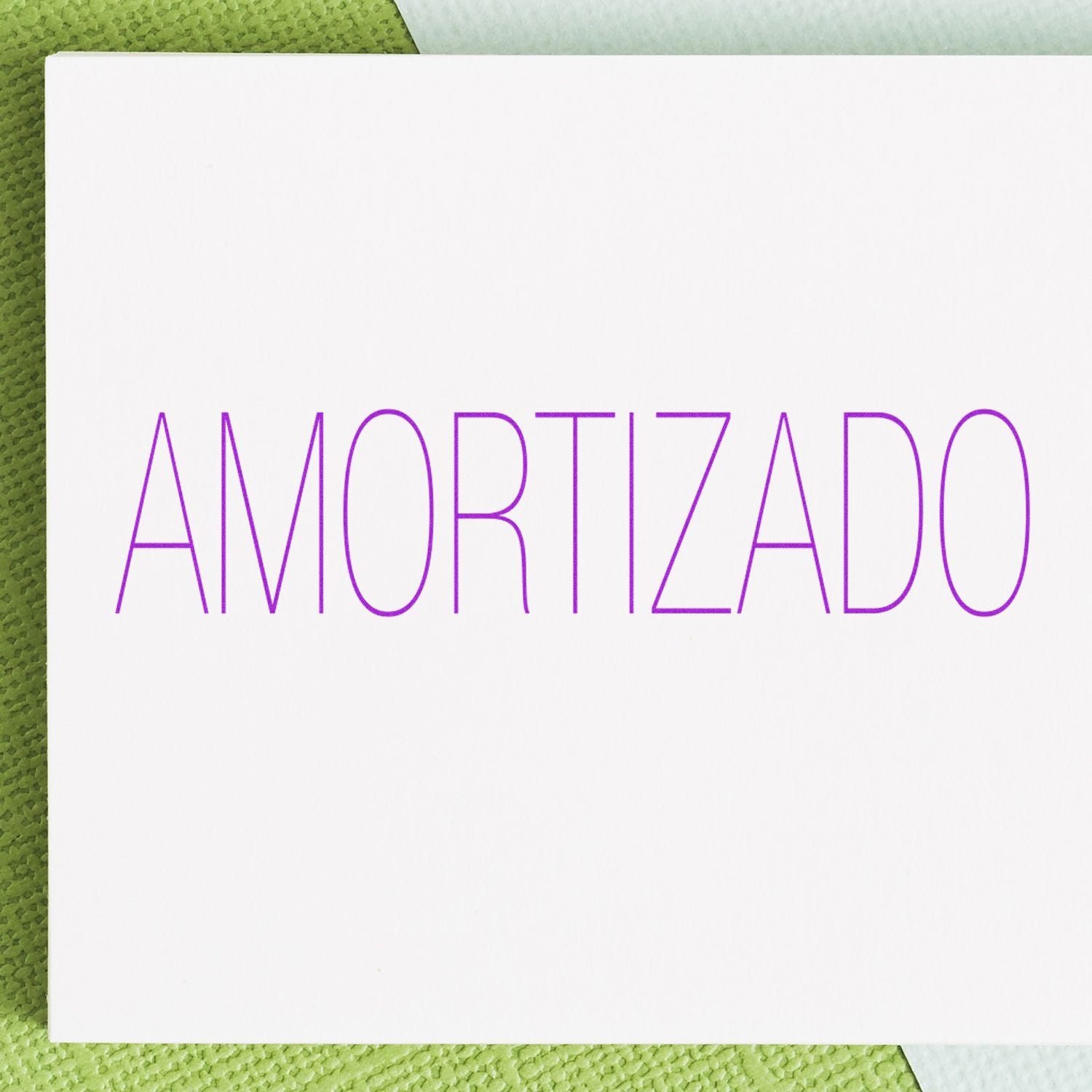 Amortizado rubber stamp impression in purple ink on a white card, placed on a green textured surface.