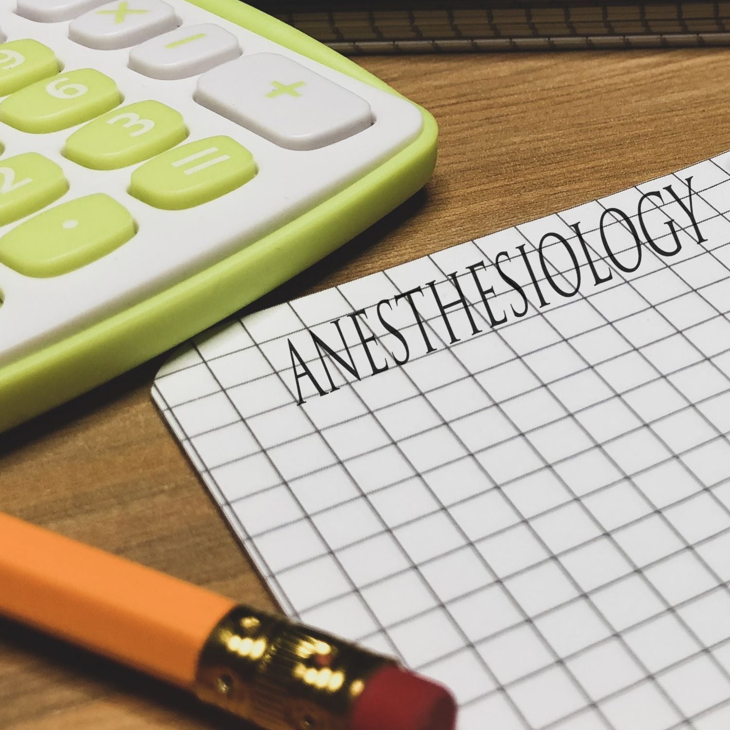 Self Inking Amortizado Stamp imprinting ANESTHESIOLOGY on graph paper, next to a pencil and a calculator on a wooden desk.