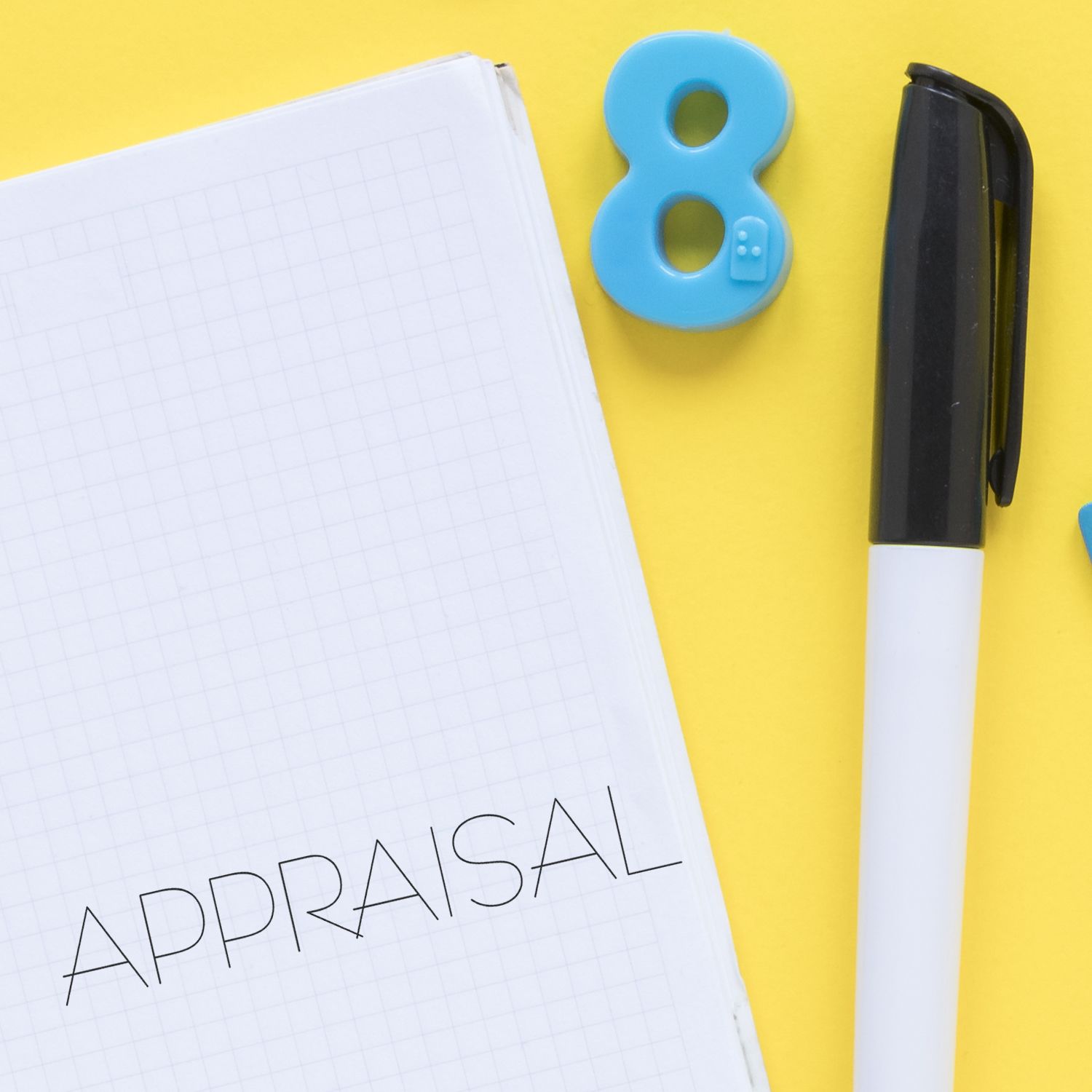 Large Self Inking Appraisal Stamp in use on a notepad with the word APPRAISAL stamped, alongside a pen and a blue number 8 on a yellow background.