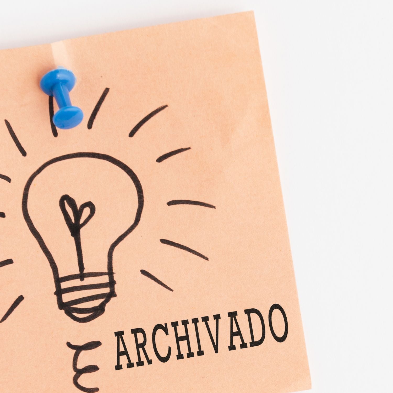 Archivado rubber stamp on a sticky note with a lightbulb drawing, pinned to a board with a blue pushpin.