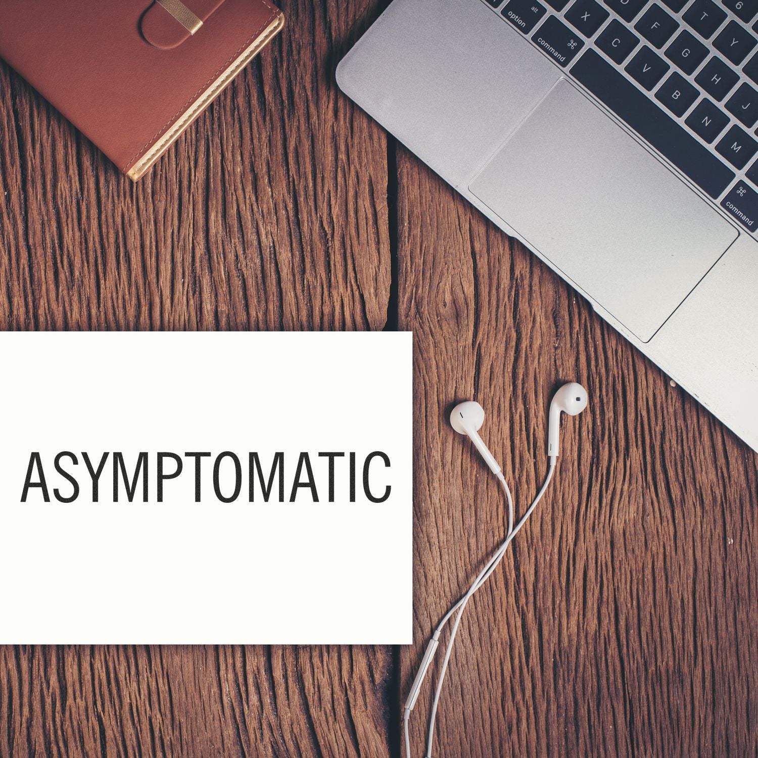 Asymptomatic rubber stamp on white paper next to a laptop, earphones, and a brown notebook on a wooden surface.