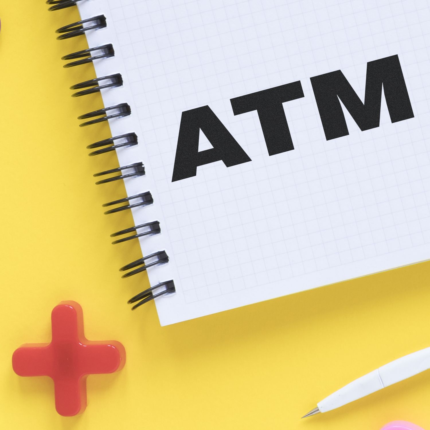 Large Pre Inked ATM Stamp on a spiral notebook with a yellow background, red cross symbol, and a white pen.