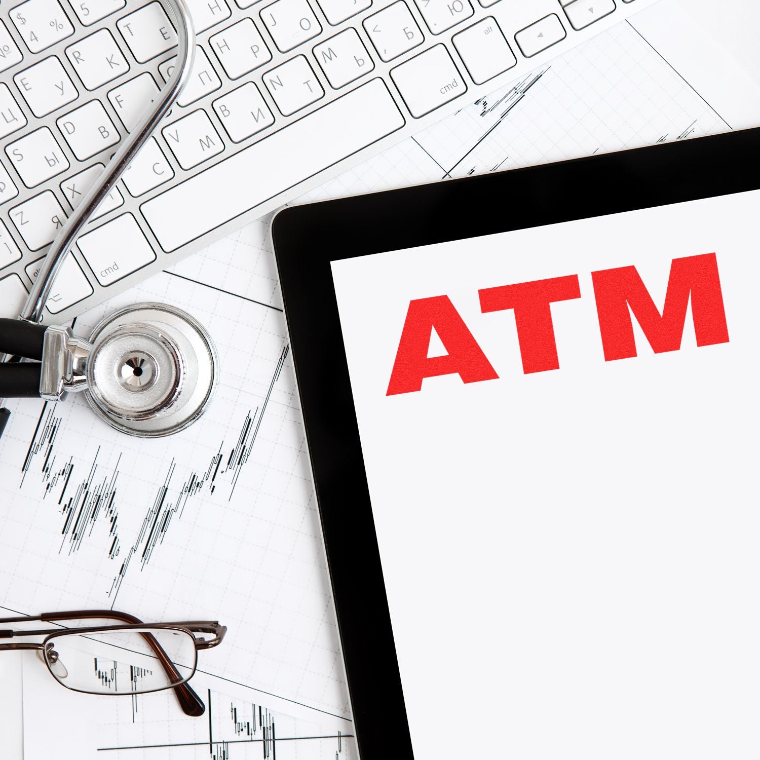 Large ATM Rubber Stamp in use on a white paper, surrounded by a keyboard, stethoscope, glasses, and financial charts.