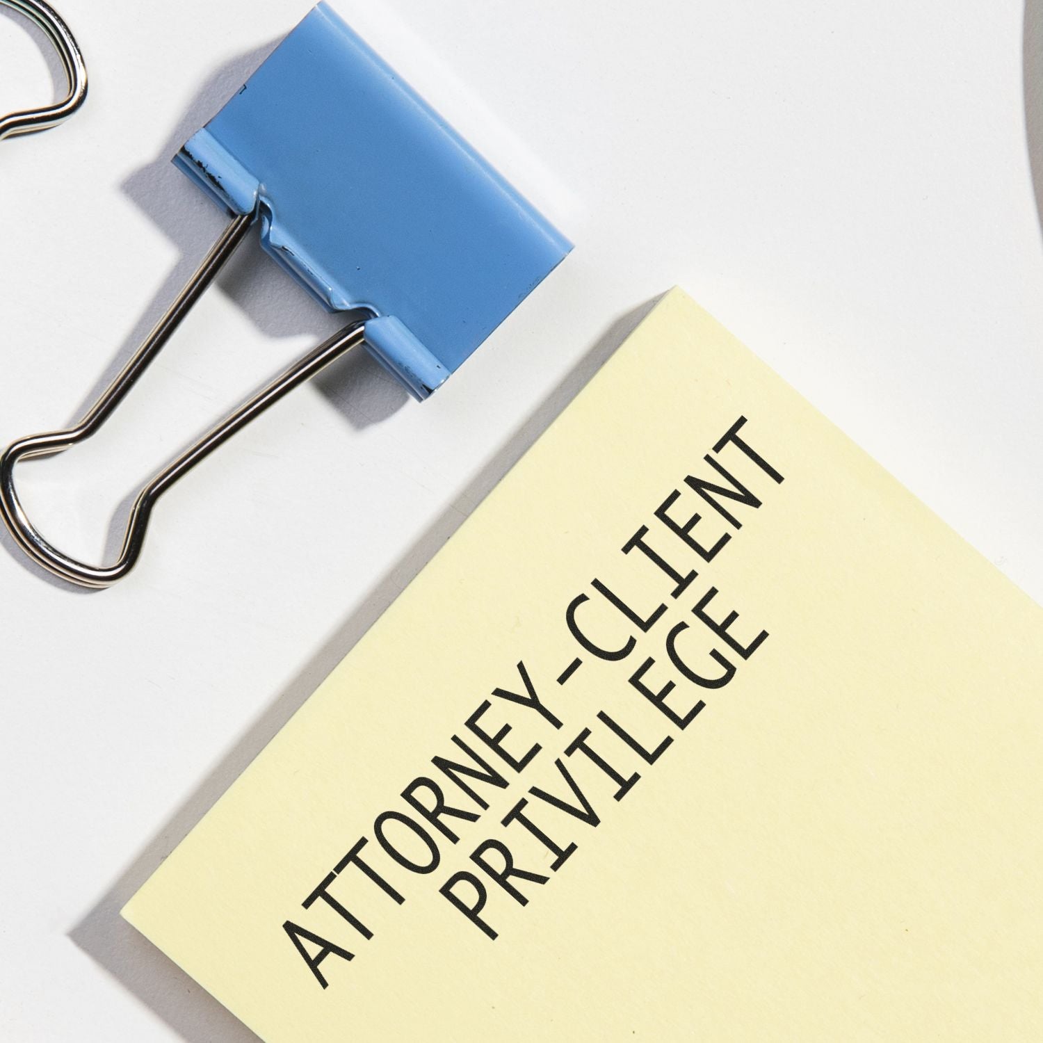 Attorney Client Privilege rubber stamp on a yellow paper next to a blue binder clip.