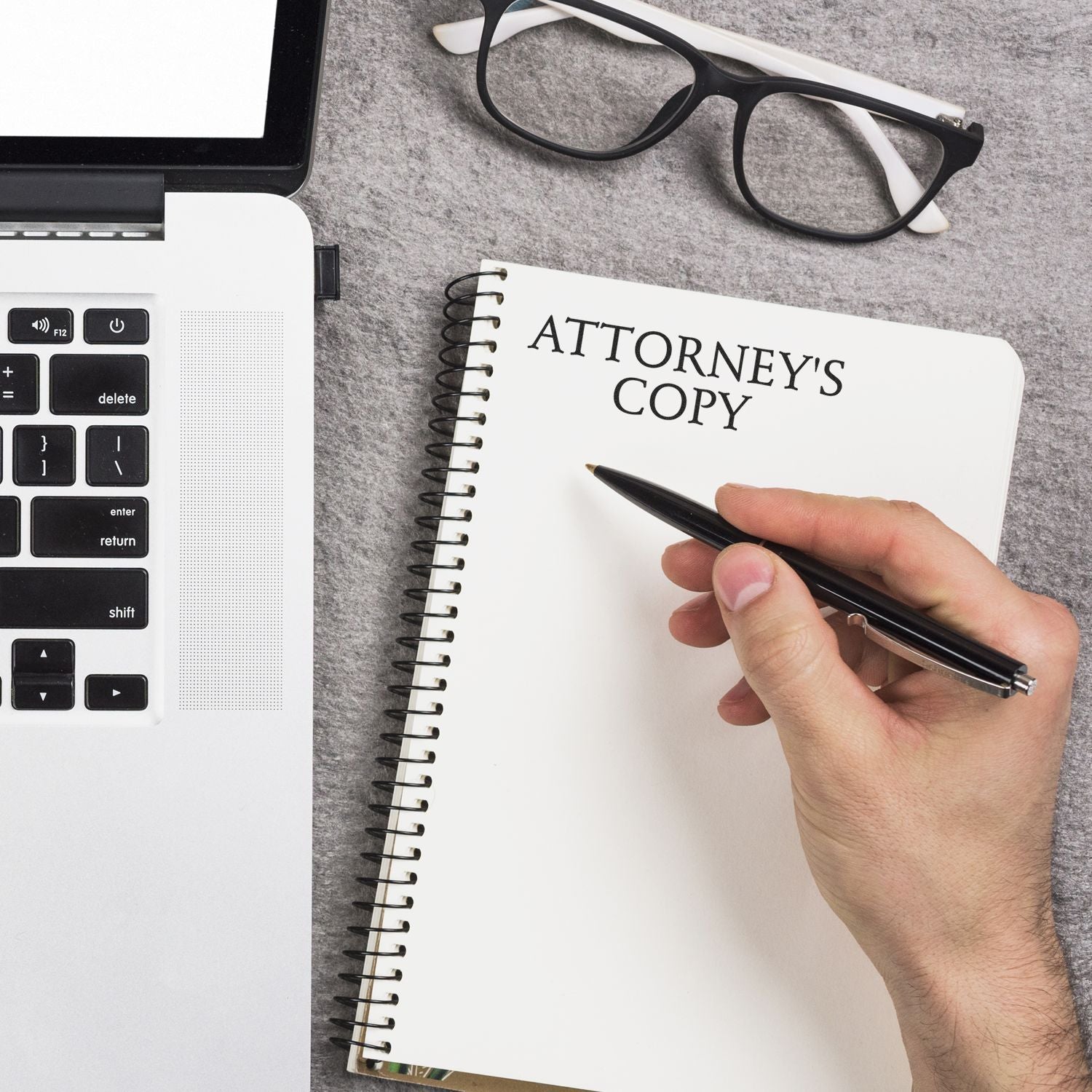 Hand holding pen near notebook labeled ATTORNEY'S COPY beside a laptop and glasses, showcasing the Slim Pre-Inked Attorney's Copy Stamp.