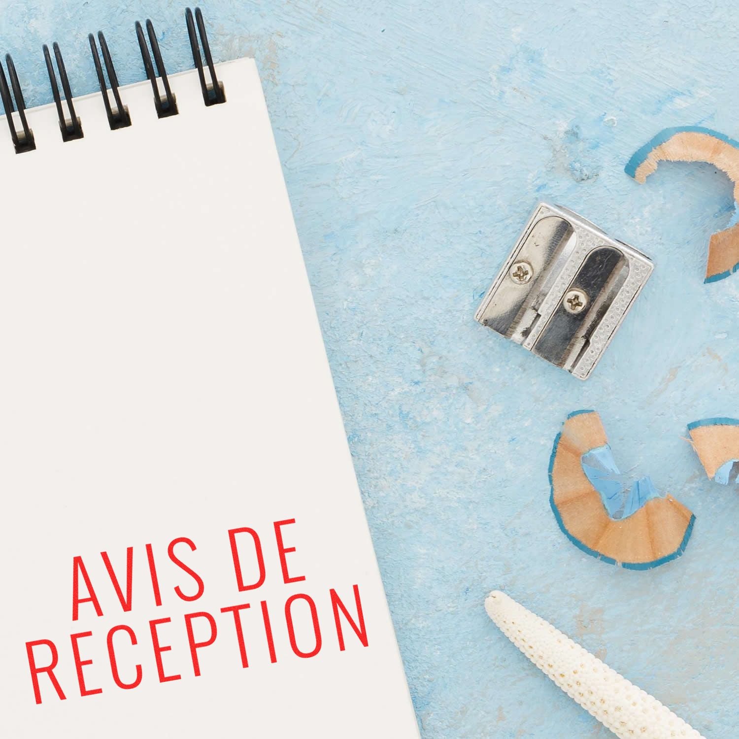 Avis De Reception rubber stamp on a white notepad with a pencil sharpener and shavings on a light blue background.