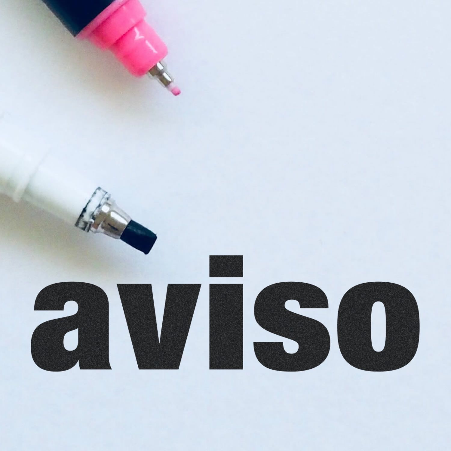 Two markers, one pink and one white, with the word "aviso" stamped in bold black letters using the Aviso Rubber Stamp on a white surface.