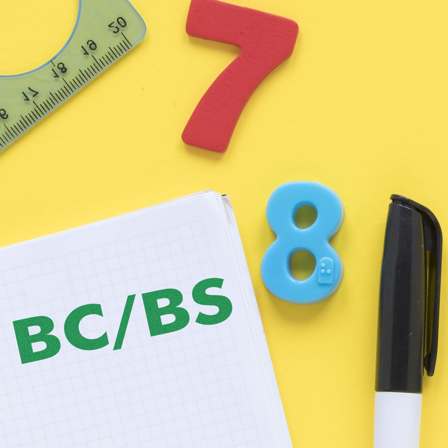 Large BC/BS Rubber Stamp in use on a notepad with a pen, ruler, and colorful numbers on a yellow background.