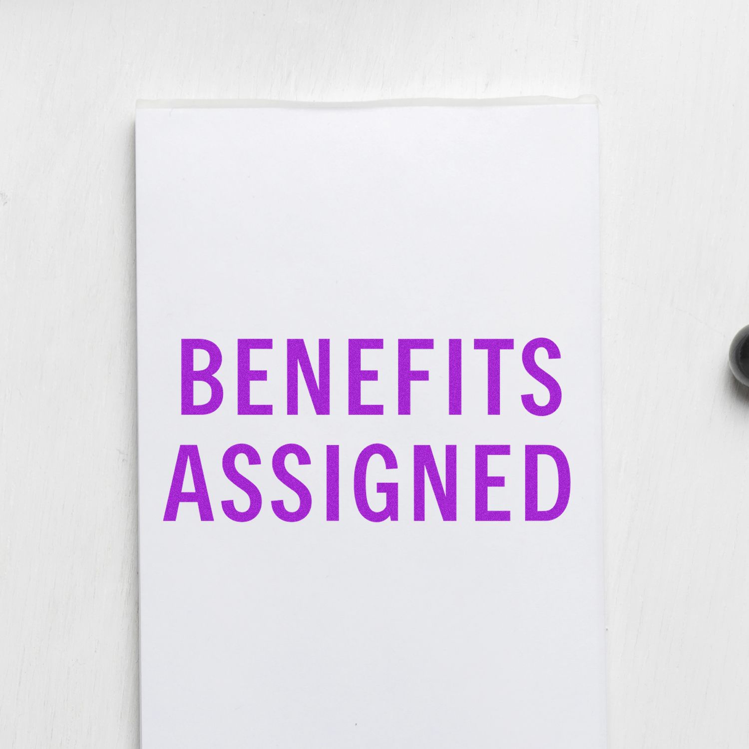 Benefits Assigned rubber stamp in purple ink on white paper, partially visible black stamp handle on the right side.