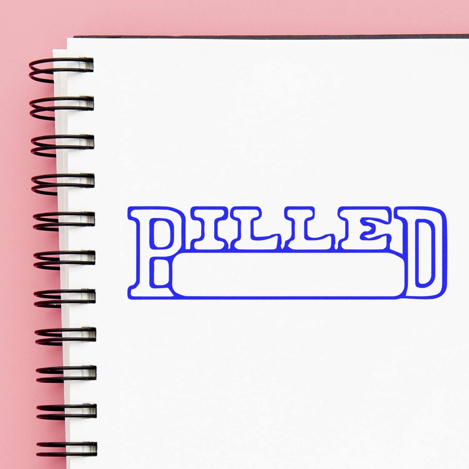 Large Self Inking Billed with Date Box Stamp in blue ink on a white spiral notebook with a pink background.