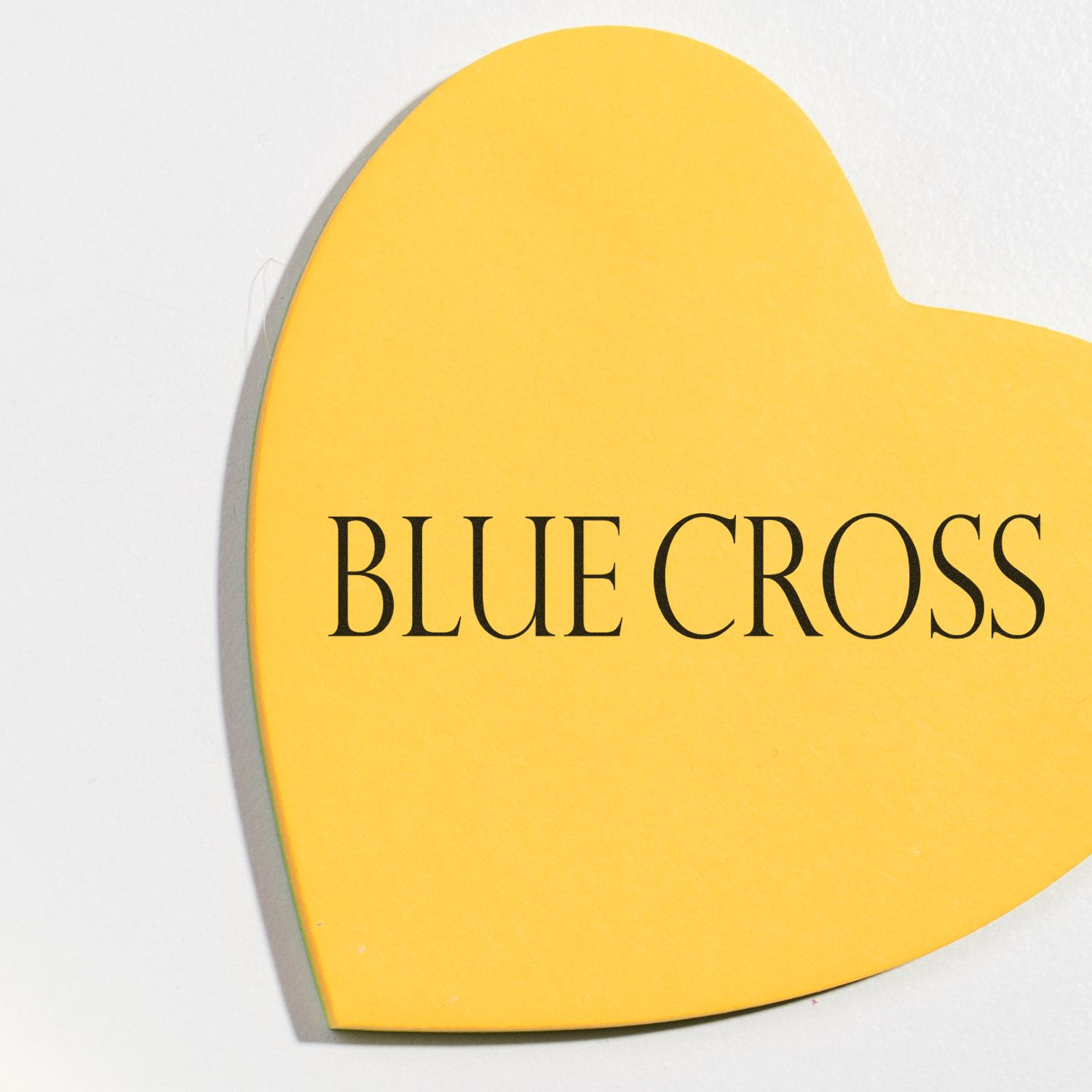 Yellow heart-shaped paper with BLUE CROSS text, stamped using a Blue Cross Rubber Stamp, placed on a white surface.