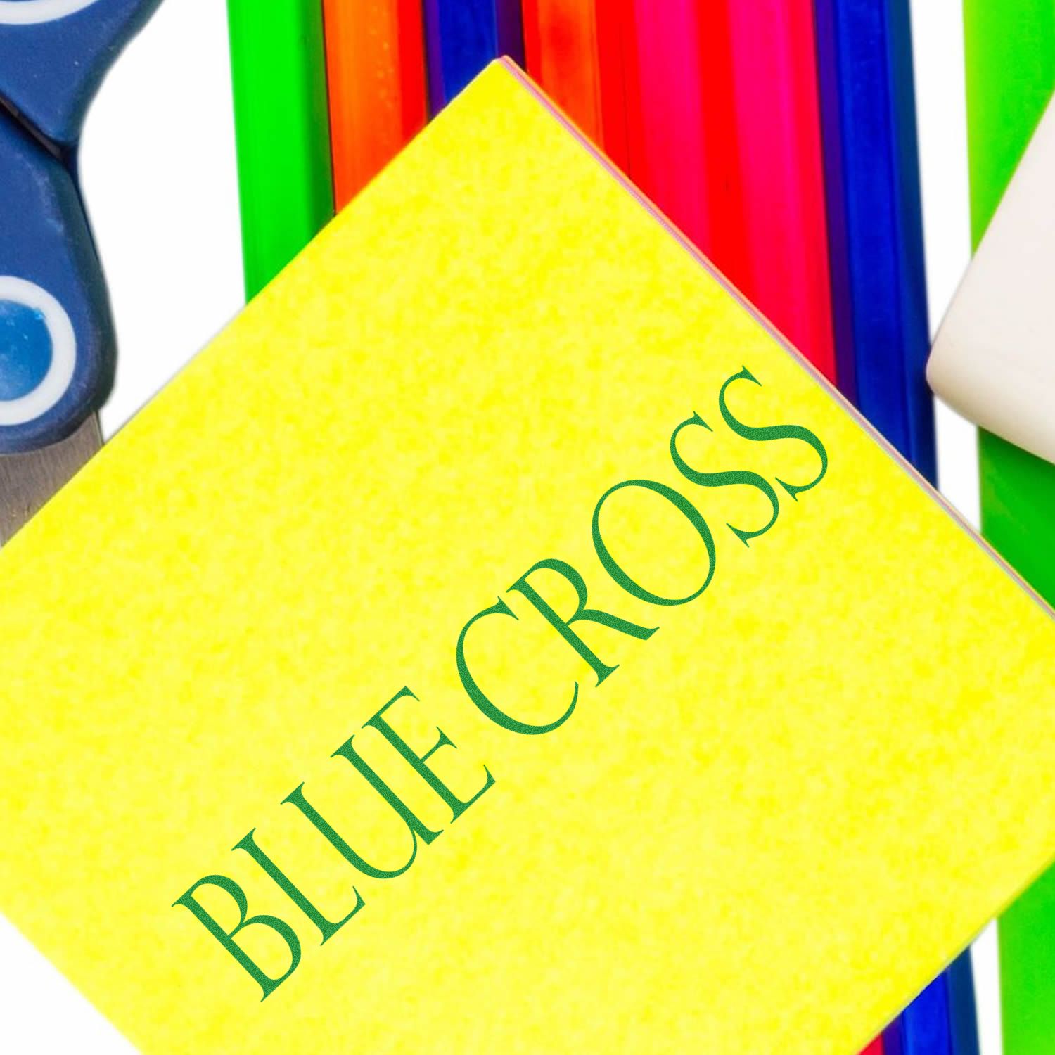 Slim Pre-Inked Blue Cross Stamp on a yellow paper, surrounded by colorful stationery items including scissors and rulers.