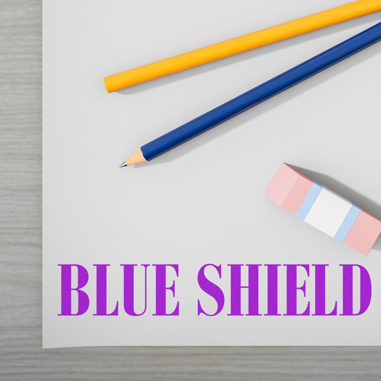 Large Self Inking Blue Shield Stamp imprint on paper with a pencil, pen, and eraser nearby on a wooden desk.