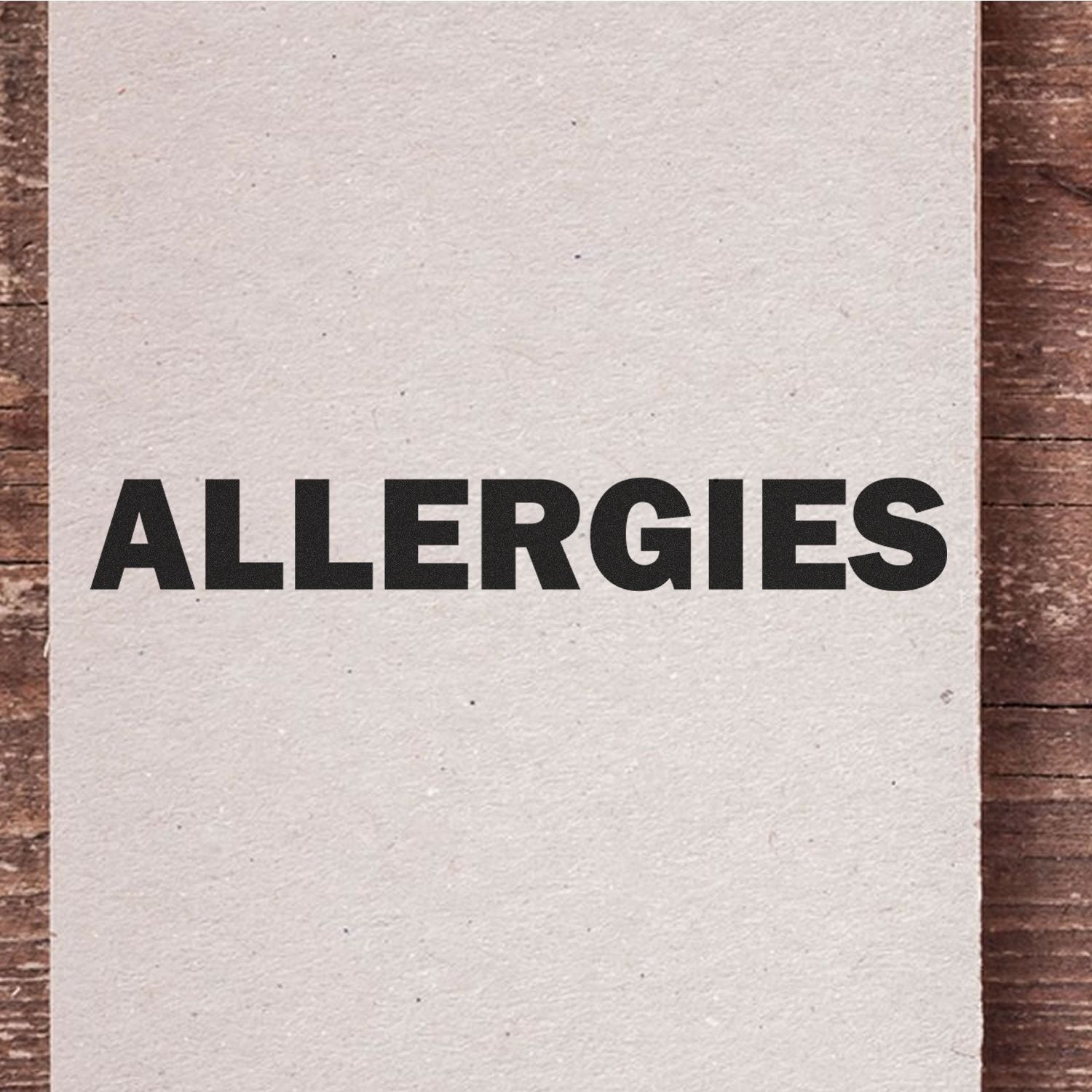 Bold Allergies Rubber Stamp on a white paper, placed on a wooden surface. The word ALLERGIES is stamped in large, bold black letters.