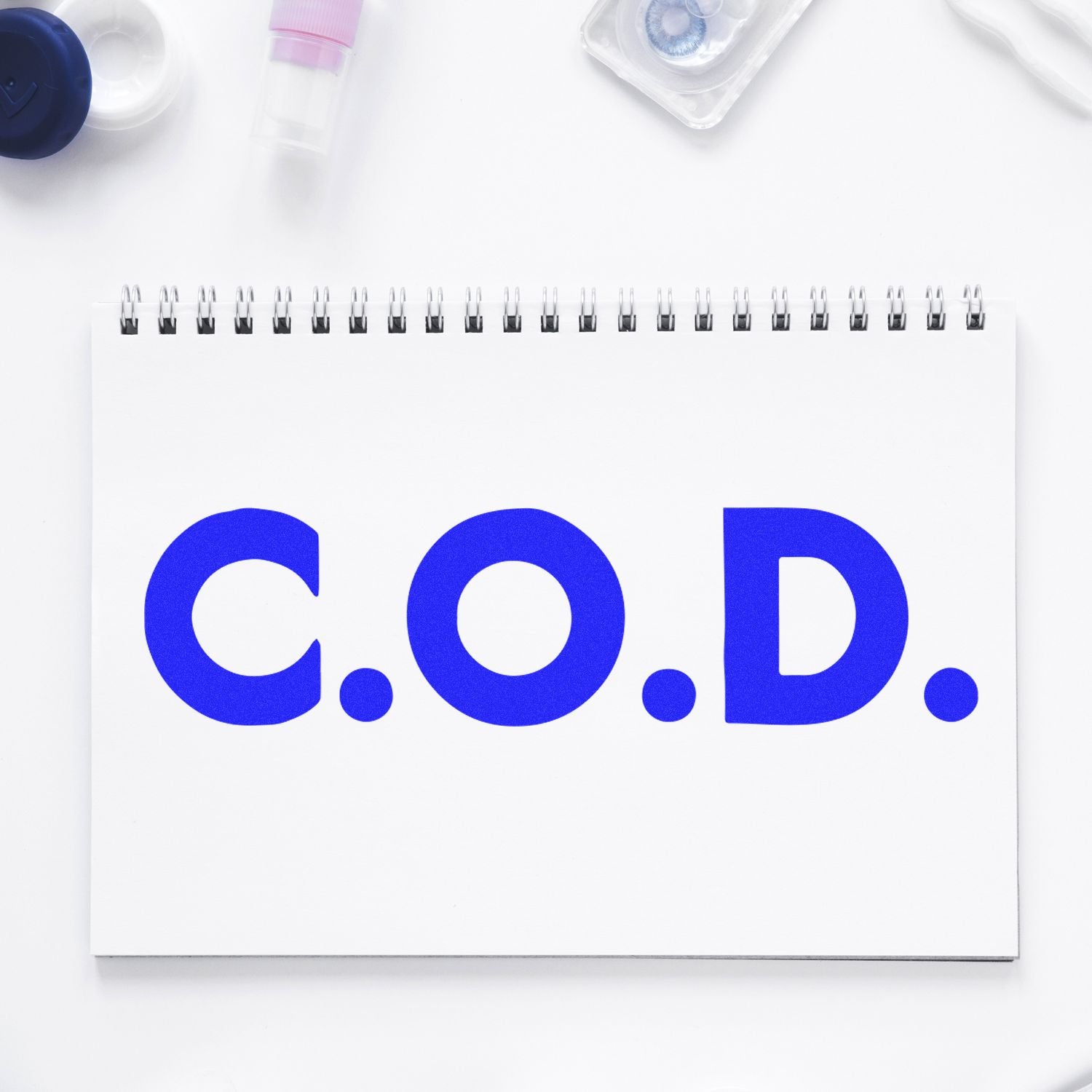 A notebook with C.O.D. stamped in bold blue letters using a Bold COD Rubber Stamp, surrounded by office supplies.