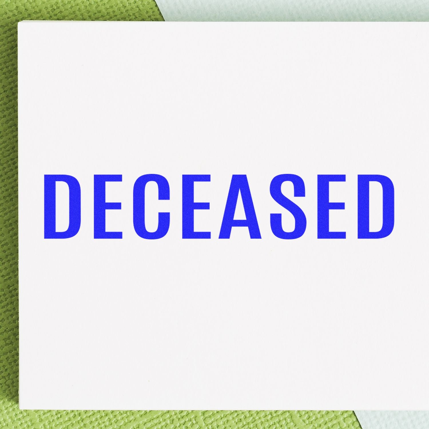 A white paper stamped with DECEASED in bold blue letters using the Large Self Inking Bold Deceased Stamp, placed on a green surface.