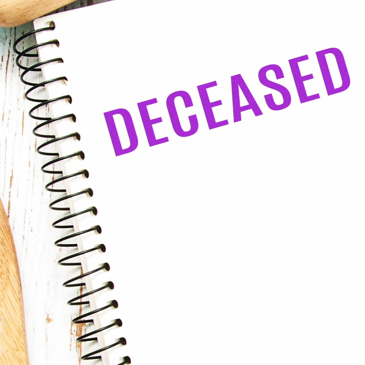 Large Self Inking Bold Deceased Stamp in purple ink on a white spiral notebook, placed on a wooden surface.