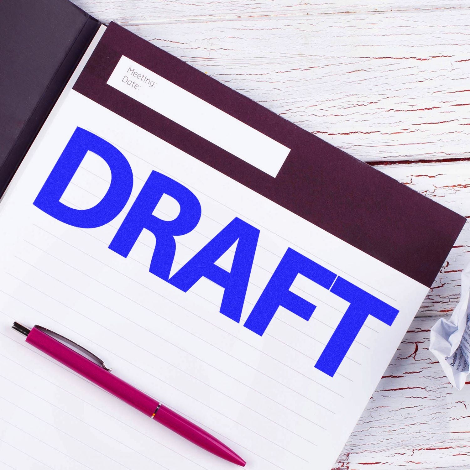 Large Bold Draft Rubber Stamp in blue ink on a notebook page with a red pen beside it, placed on a white wooden surface.