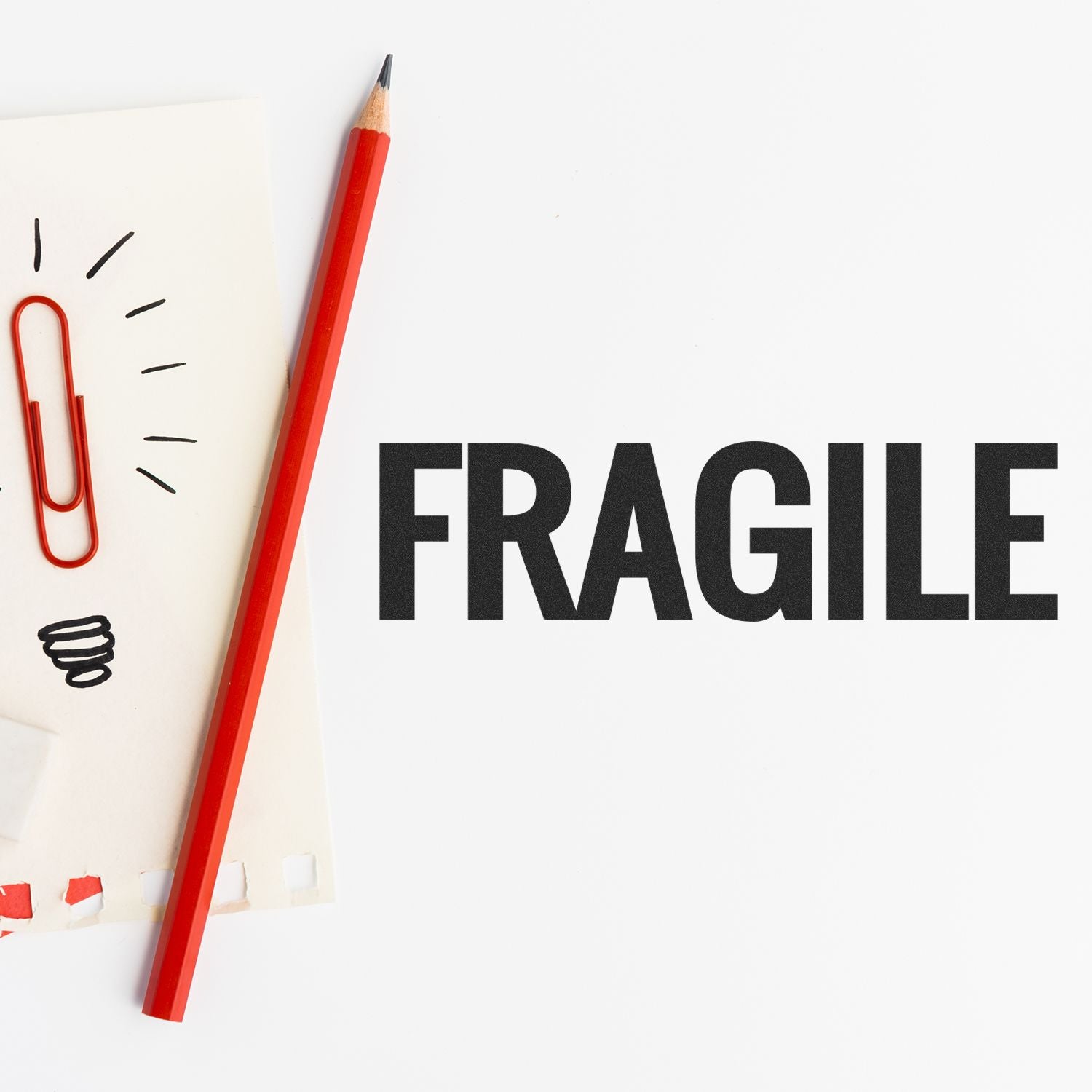 Red pencil and paper with a red paperclip next to a stamped FRAGILE text using the Large Bold Fragile Pre-Inked Stamp on a white background.