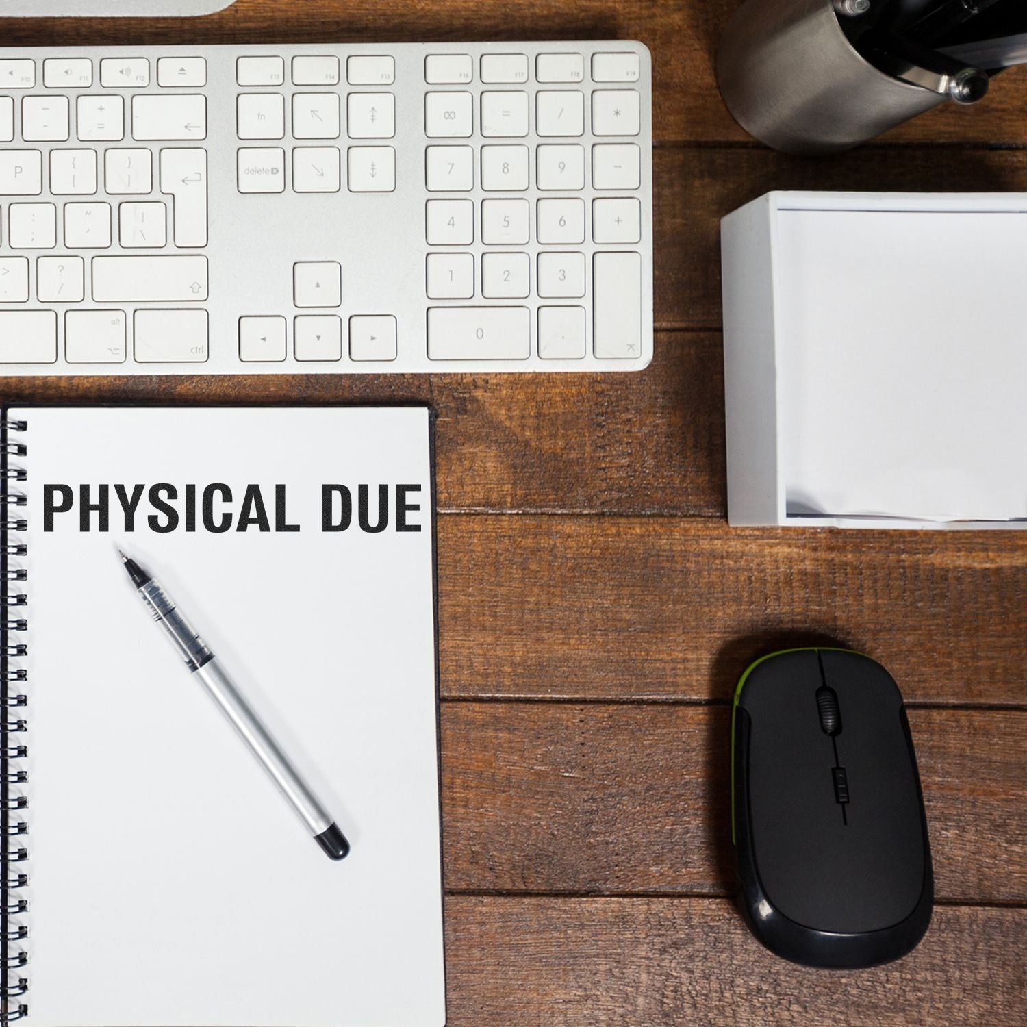 Self Inking Bold Physical Due Stamp used on a notebook, placed on a wooden desk with a keyboard, mouse, pen, and other office supplies.