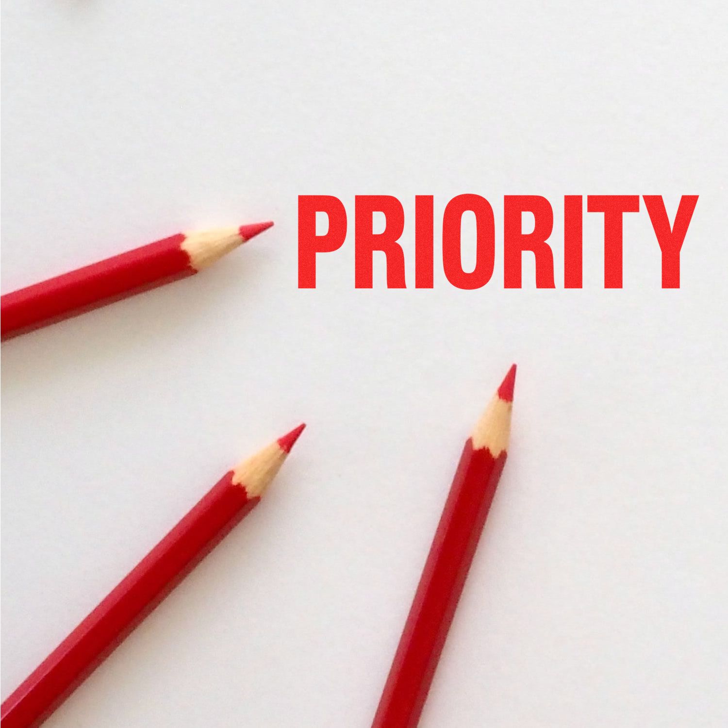 Three red pencils pointing towards the word PRIORITY stamped in bold red letters using the Large Bold Priority Rubber Stamp.