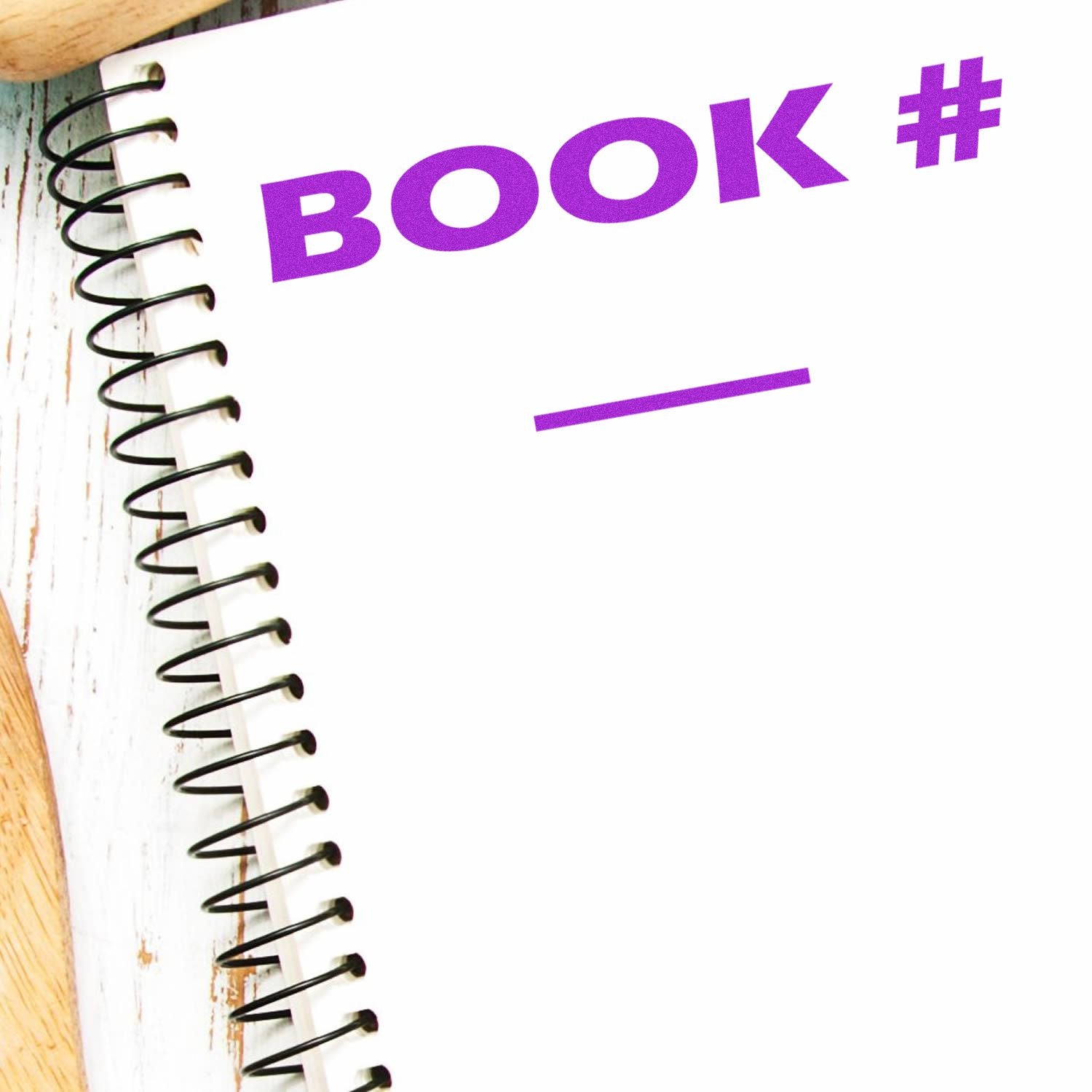 Slim Pre-Inked Book Stamp imprint on a white spiral notebook with BOOK # in purple text and a blank line below.