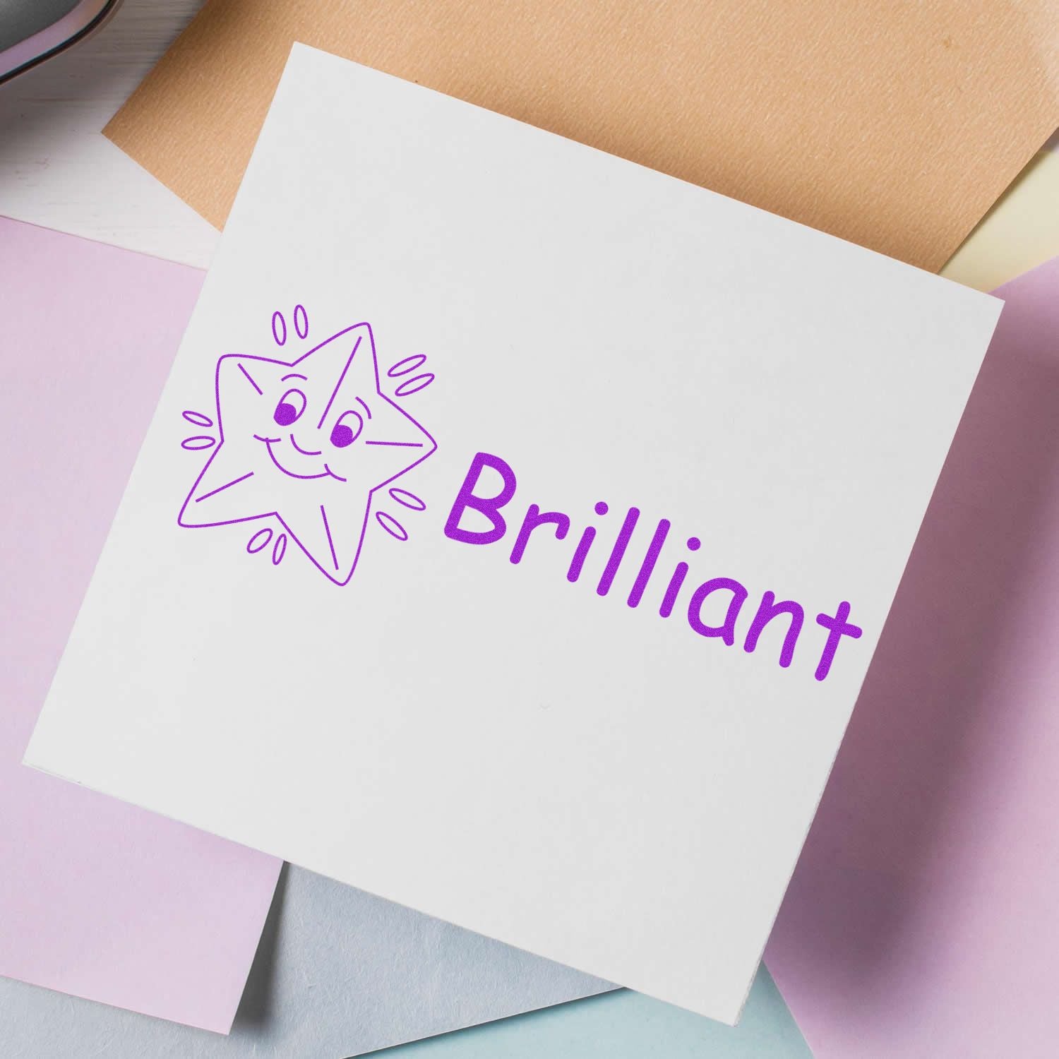 White paper stamped with a purple smiling star and the word 'Brilliant' using a Slim Pre-Inked Brilliant Stamp, surrounded by pastel papers.