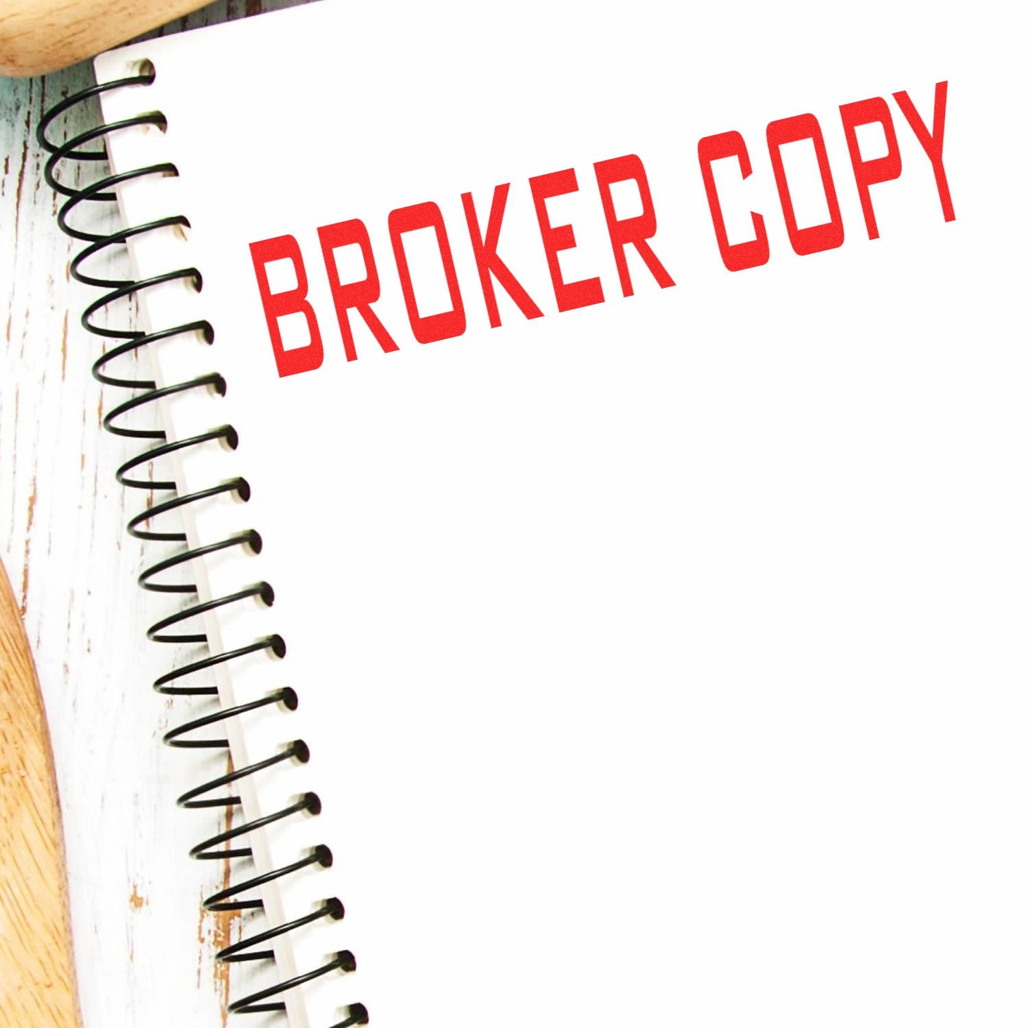 Slim Pre-Inked Broker Copy Stamp in red ink on a white spiral notebook, placed on a wooden surface.